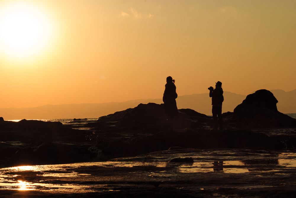 Silhouette of a man taking a sunset photo while a young girl looks on.